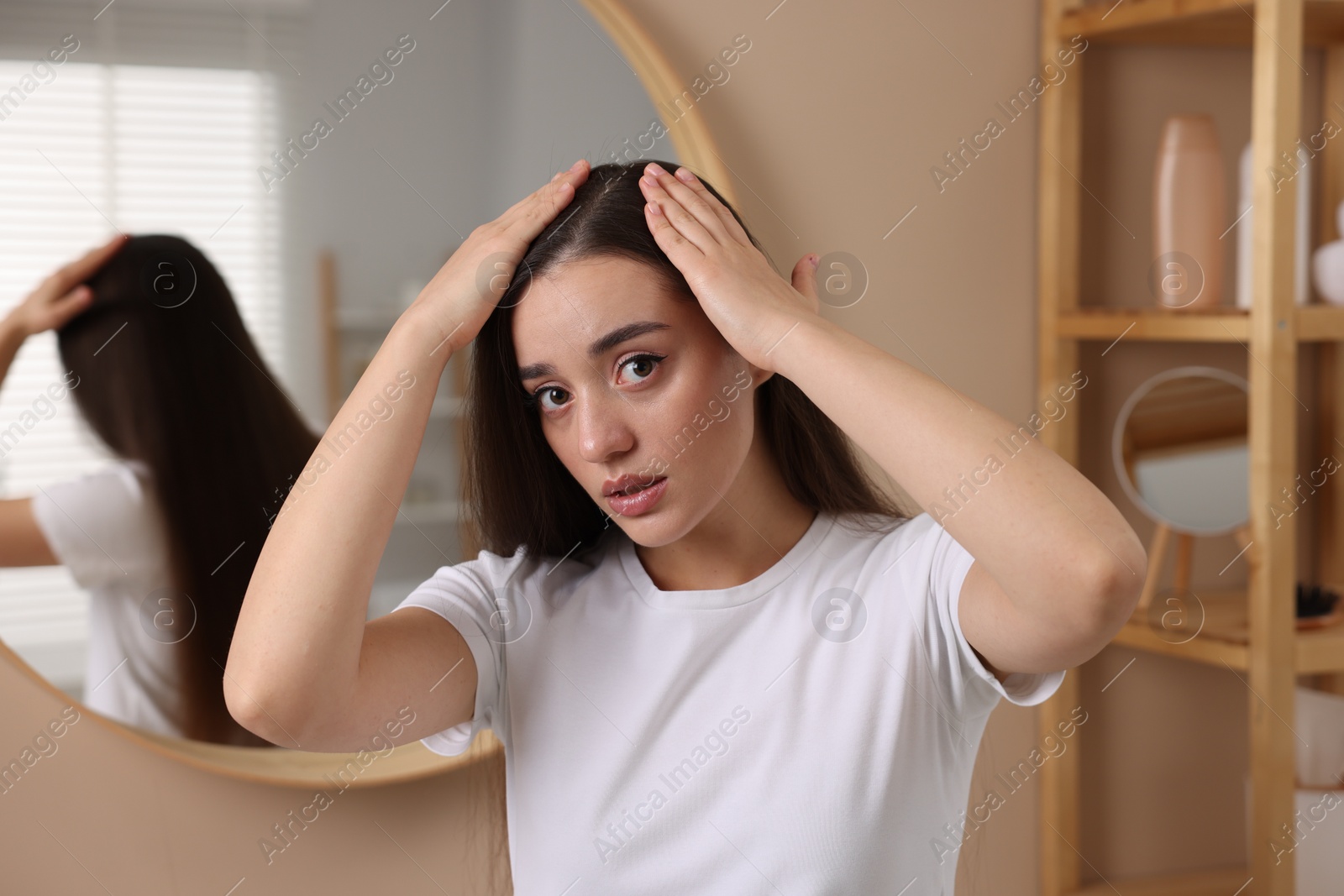 Photo of Woman examining her hair and scalp in bathroom. Dandruff problem