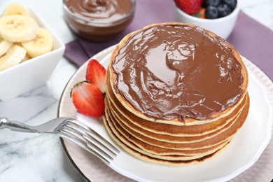 Photo of Tasty pancakes with chocolate paste and berries on white marble table