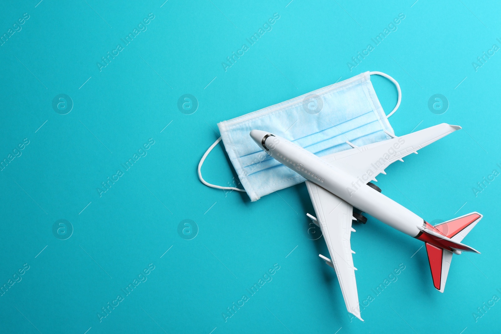 Photo of Toy airplane and protective mask on light blue background, flat lay with space for text. Travelling during coronavirus pandemic