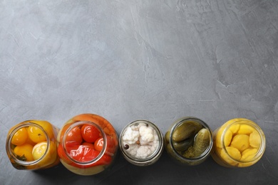Photo of Open jars of tasty pickled vegetables on grey table