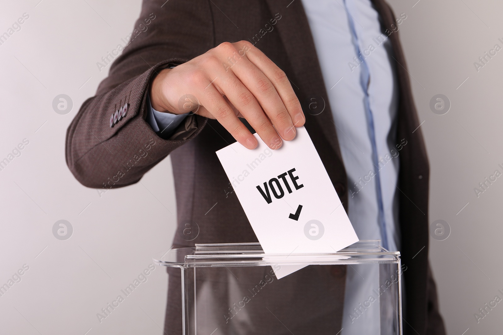 Image of Man putting paper with word Vote and tick into ballot box on light grey background