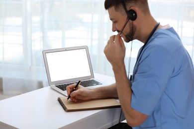 Photo of Doctor with headset consulting patient online at desk in clinic, space for text. Health service hotline