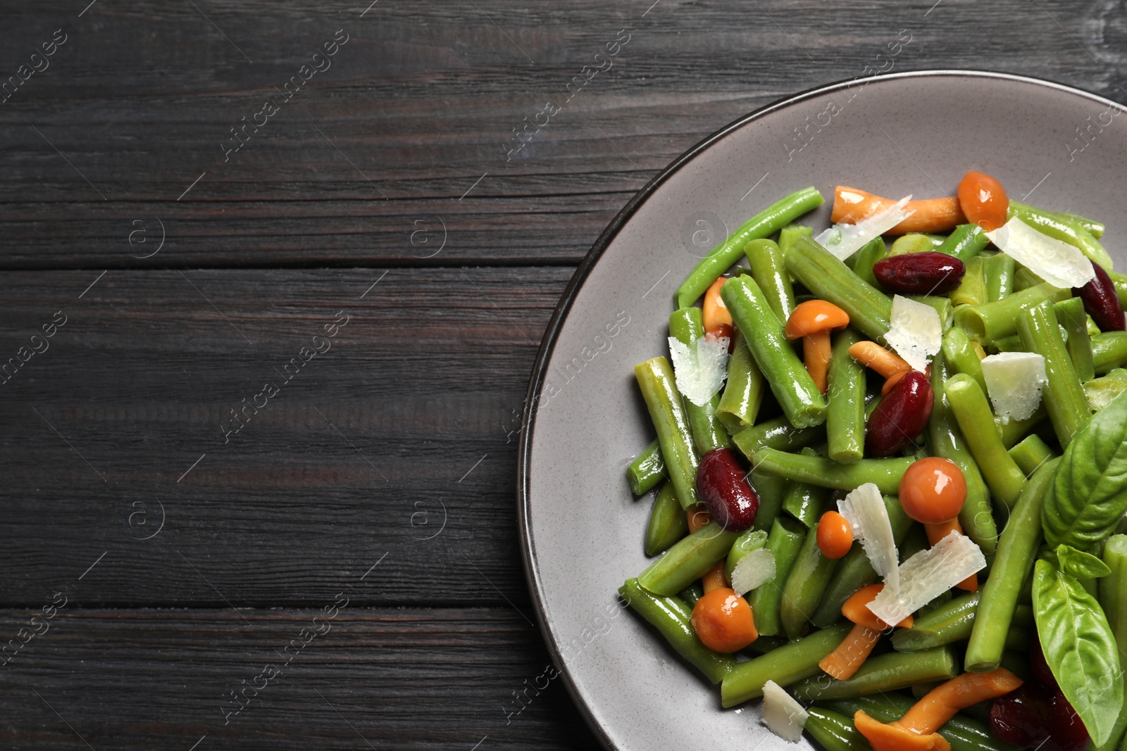 Photo of Delicious salad with green beans, mushrooms and cheese on black wooden table, top view. Space for text