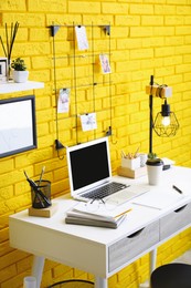 Stylish home office interior with comfortable workplace near yellow brick wall