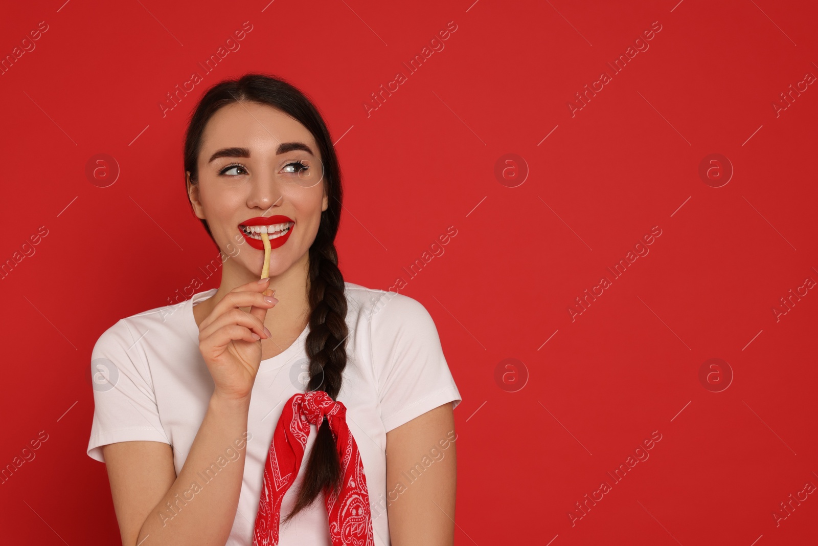 Photo of Beautiful young woman eating French fries on red background. Space for text