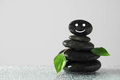 Photo of Stack of stones with drawn happy face, green leaves and water drops on table against grey background, space for text. Zen concept