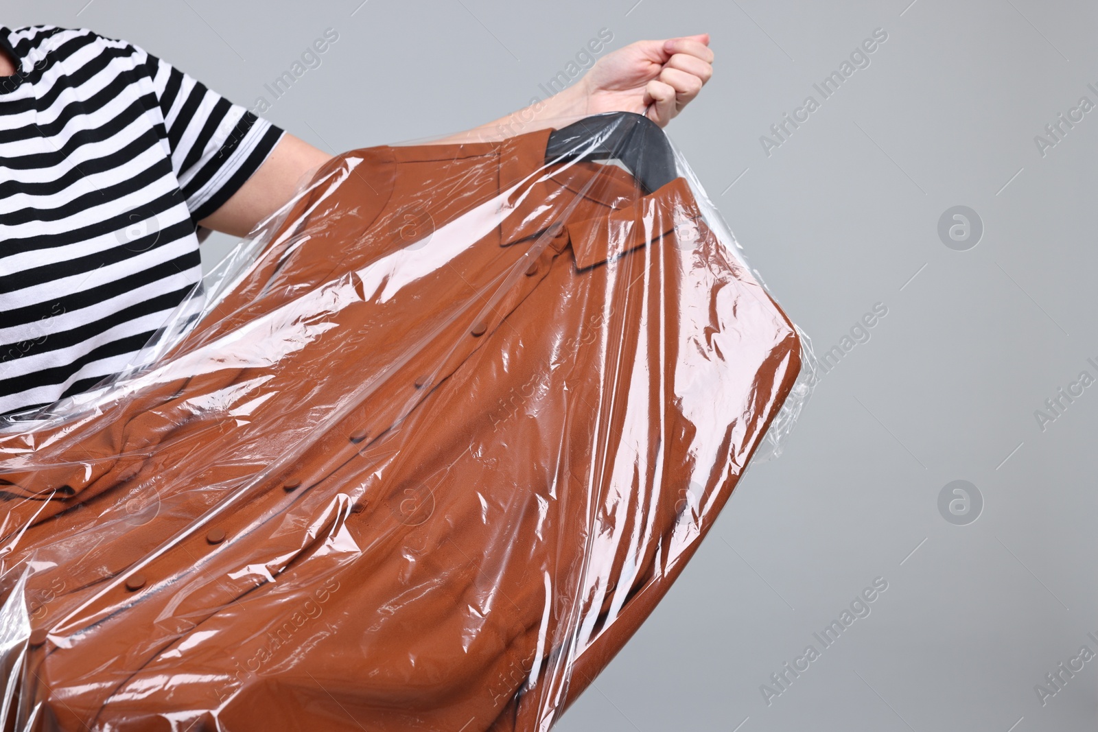 Photo of Dry-cleaning service. Woman holding shirt in plastic bag on gray background, closeup. Space for text