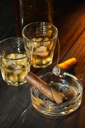 Photo of Cigars, ashtray and whiskey with ice cubes on black wooden table