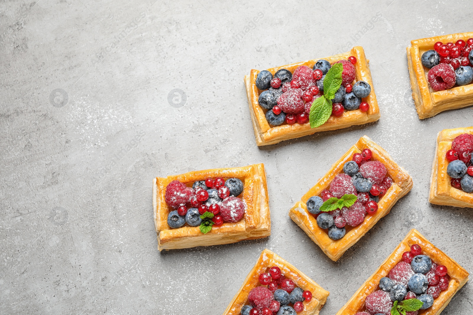 Photo of Fresh delicious puff pastry with sweet berries on grey table, flat lay. Space for text