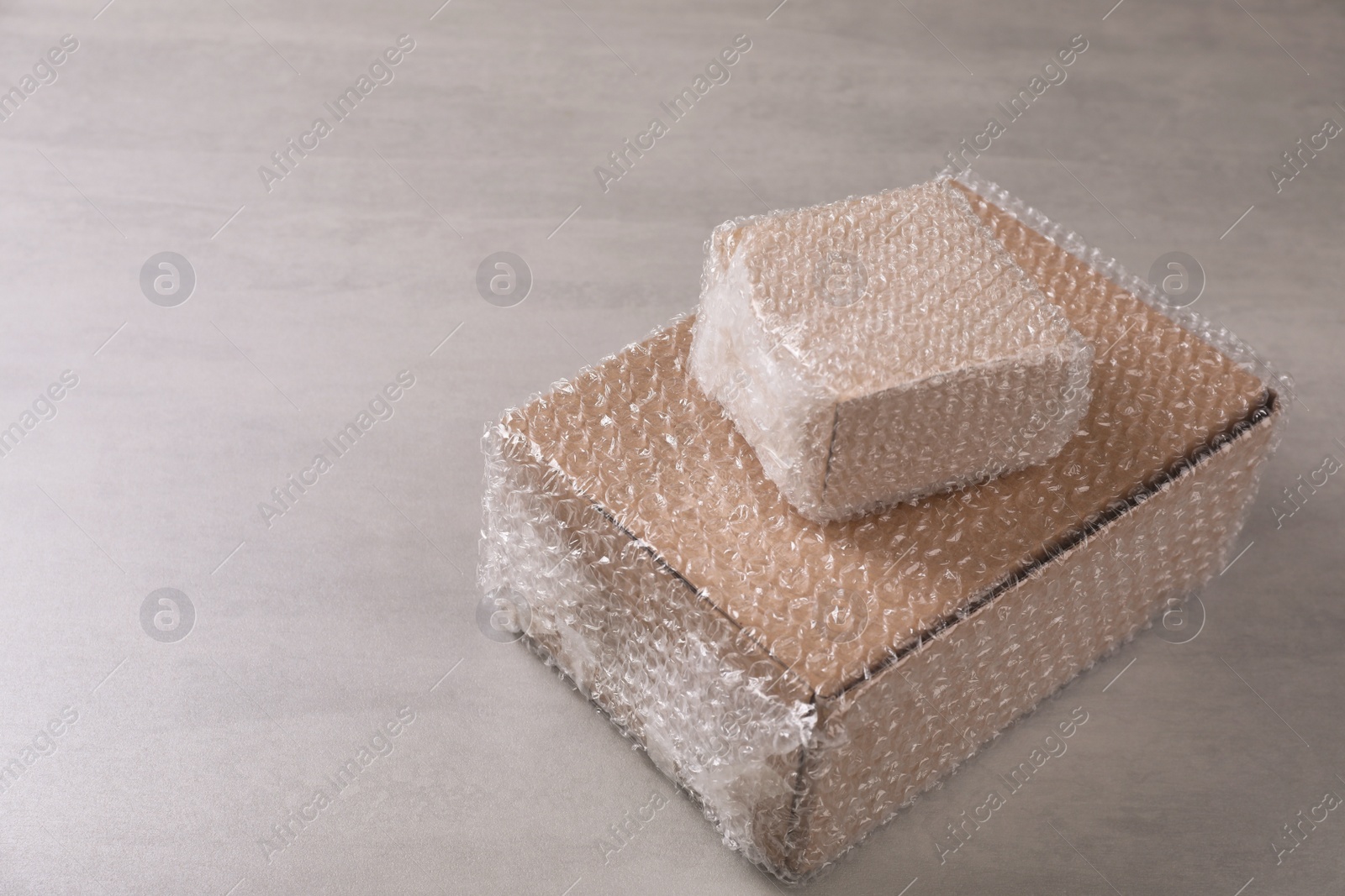 Photo of Cardboard boxes covered with bubble wrap on light grey table. Space for text