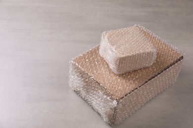 Photo of Cardboard boxes covered with bubble wrap on light grey table. Space for text