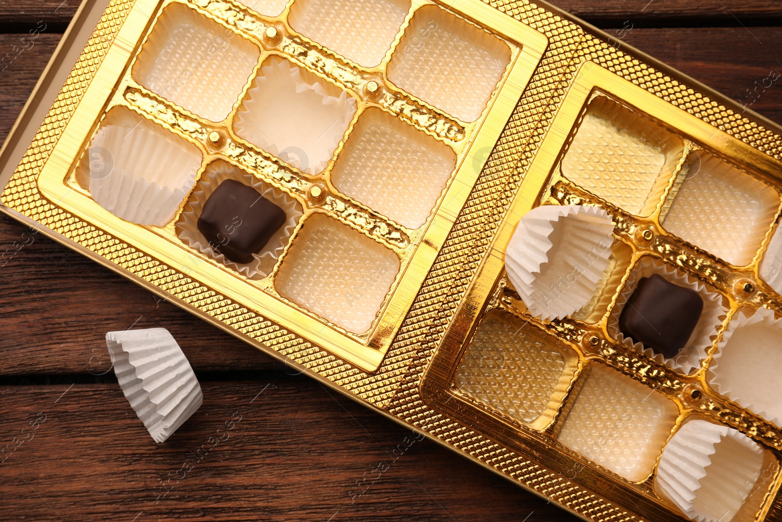 Photo of Partially empty box of chocolate candies on wooden table, flat lay