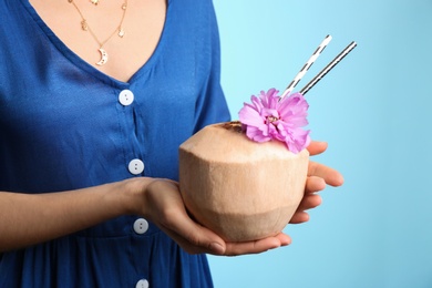 Woman holding fresh young coconut with straws on light blue background, closeup