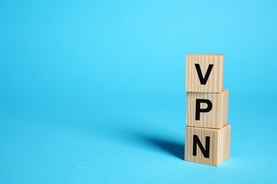 Photo of Wooden cubes with acronym VPN on light blue background, space for text
