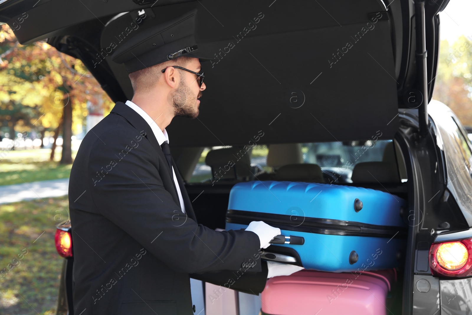 Photo of Young driver loading suitcases into car trunk outdoors