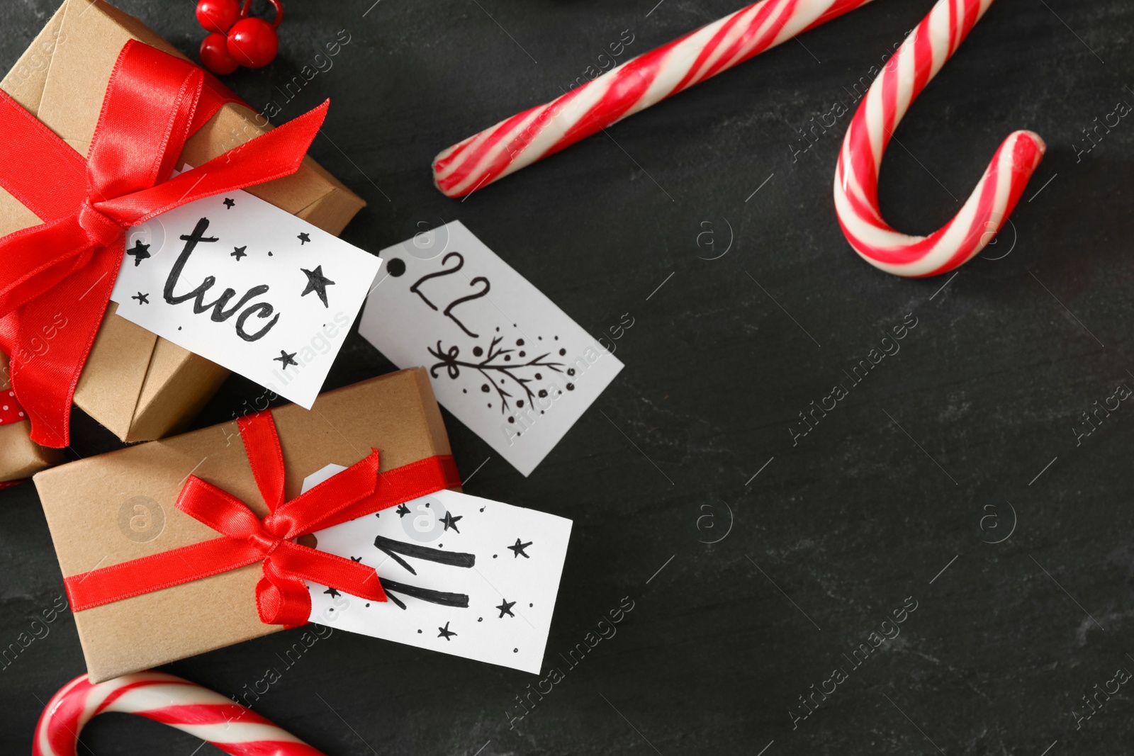 Photo of Gift boxes and Christmas candy canes on black table, flat lay. Creating advent calendar