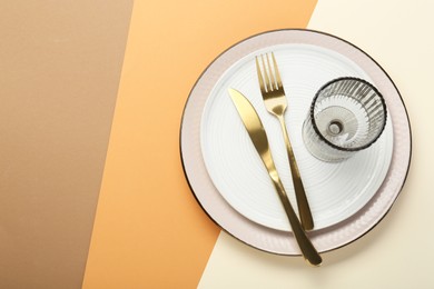 Photo of Ceramic plates, glass and cutlery on color background, top view. Space for text