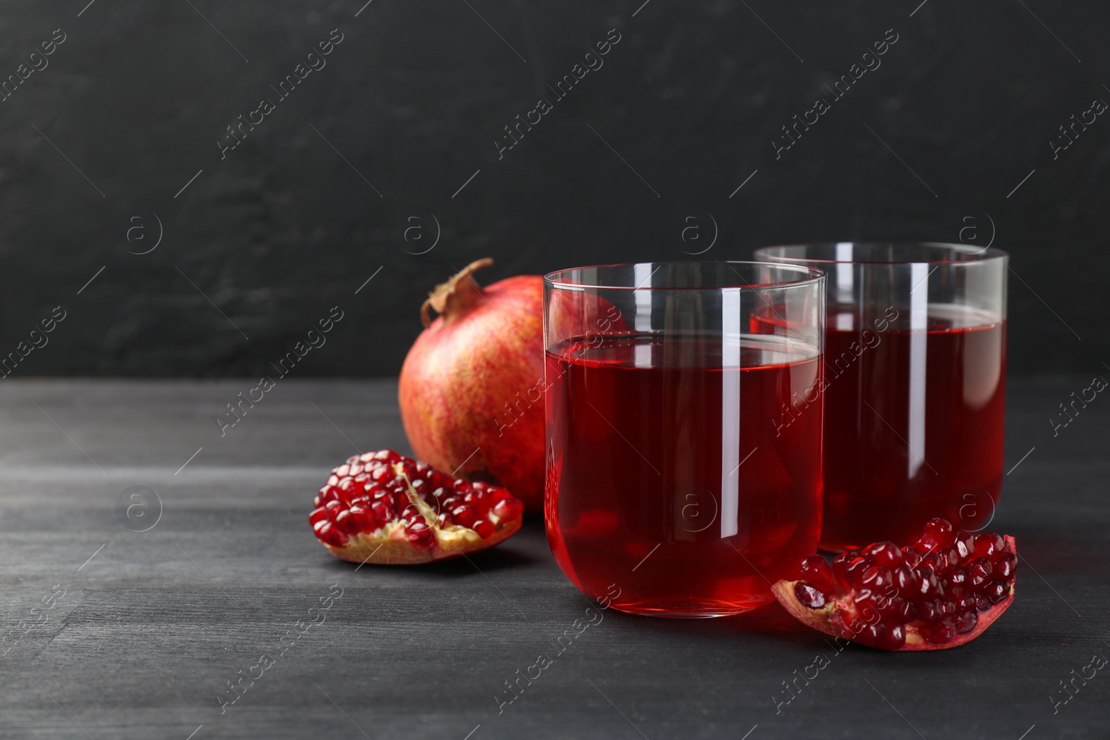 Photo of Tasty pomegranate juice in glasses and fresh fruits on black wooden table. Space for text