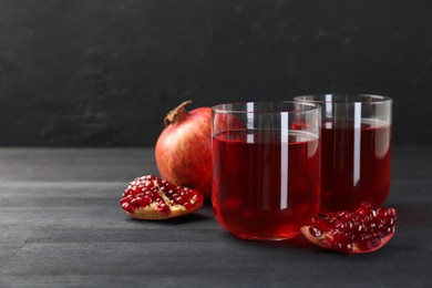 Photo of Tasty pomegranate juice in glasses and fresh fruits on black wooden table. Space for text