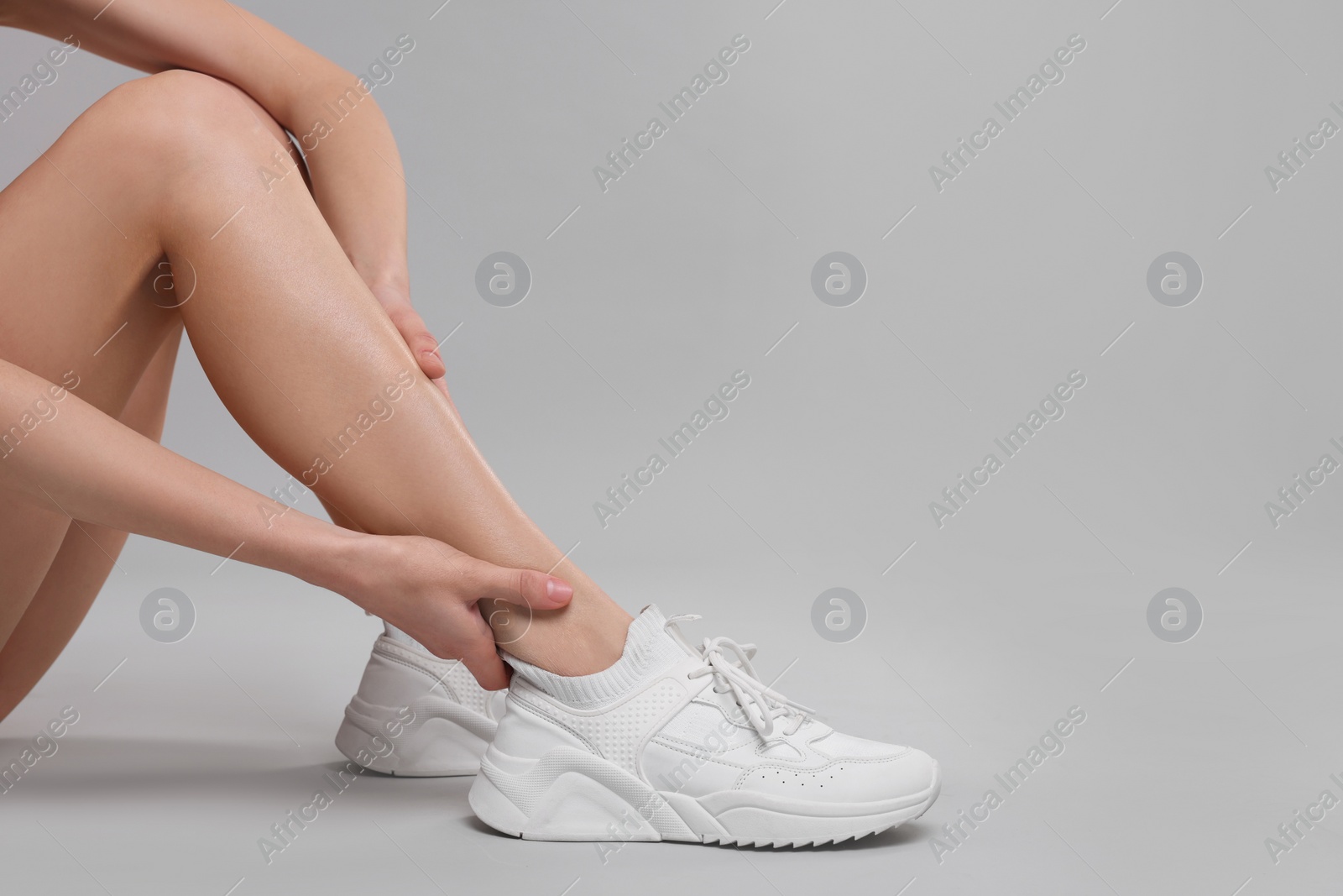Photo of Woman suffering from leg pain on grey background, closeup. Space for text