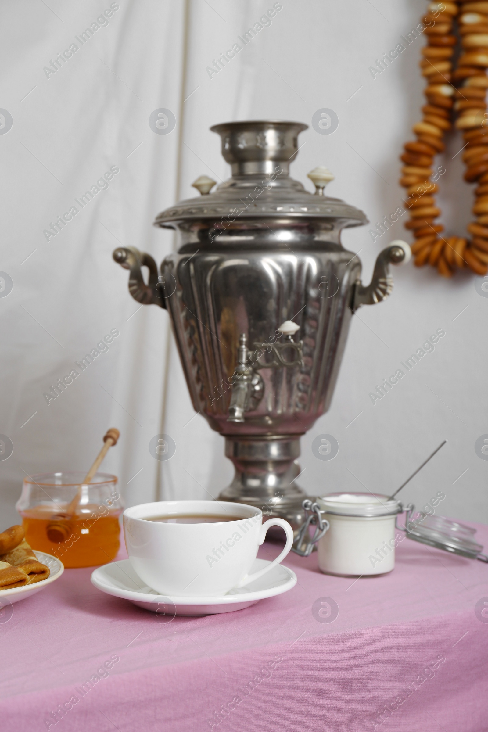 Photo of Vintage samovar, cup of hot drink and snacks served on table indoors. Traditional Russian tea ceremony