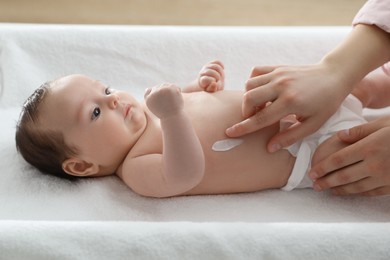 Photo of Mother applying body cream on her little baby indoors