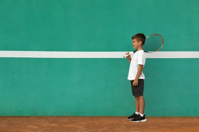 Photo of Cute little boy near green wall on tennis court. Space for text