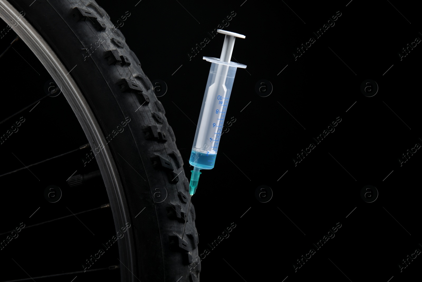 Photo of Bike wheel with syringe on black background, closeup. Using doping in cycling sport concept