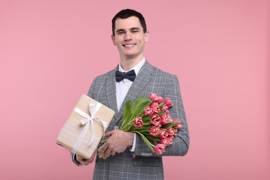 Photo of Happy young man with beautiful bouquet and present on pink background