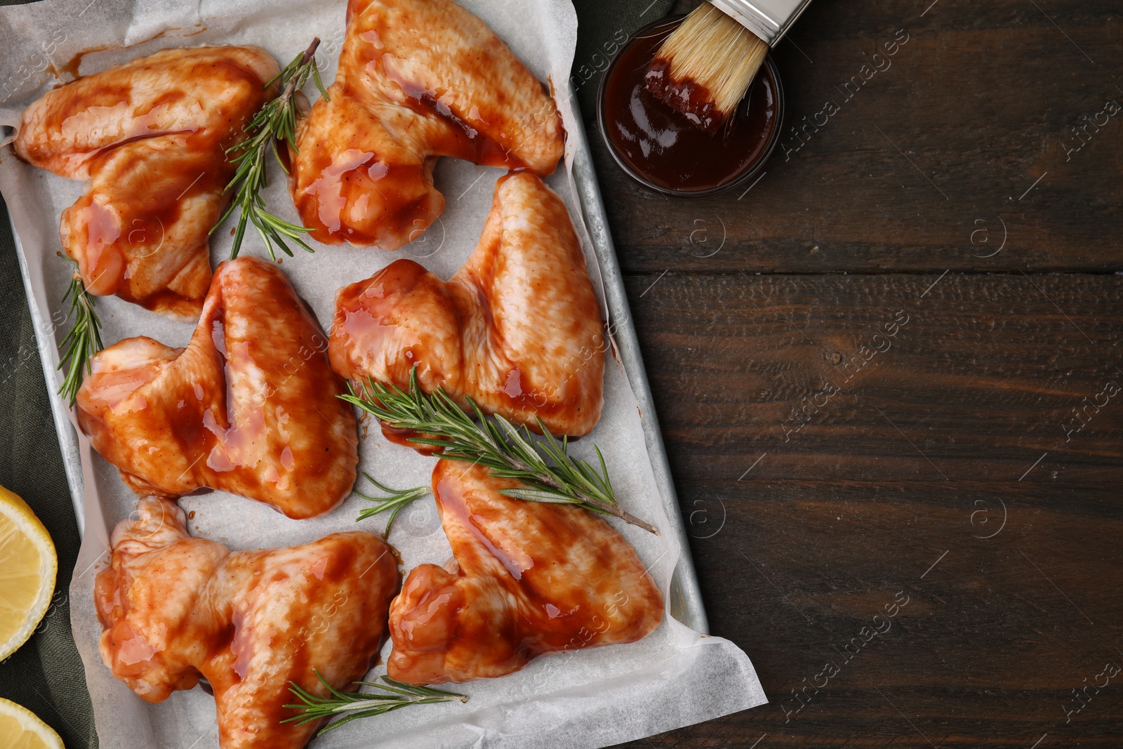 Photo of Raw chicken wings, rosemary and marinade on wooden table, flat lay. Space for text