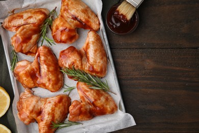 Photo of Raw chicken wings, rosemary and marinade on wooden table, flat lay. Space for text