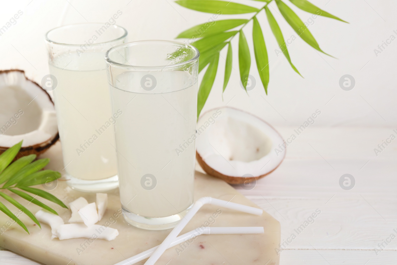 Photo of Glasses of coconut water, palm leaves and nuts on white table. Space for text