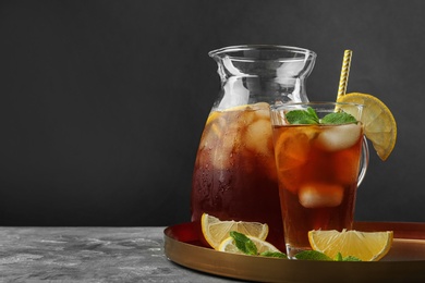 Jug and glass of delicious iced tea on grey table against black background. Space for text