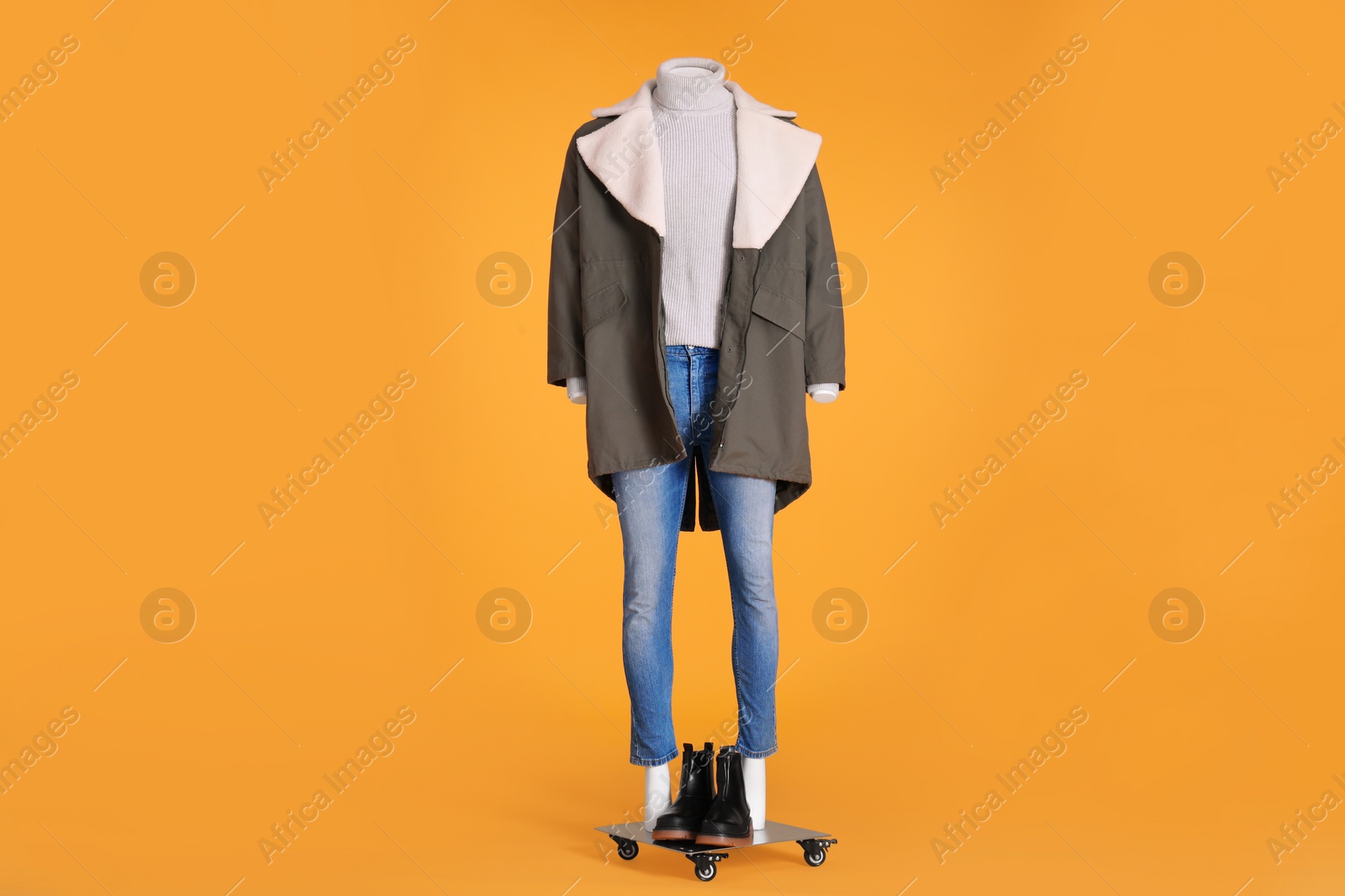 Photo of Female mannequin with boots dressed in stylish jacket, turtleneck and jeans on orange background