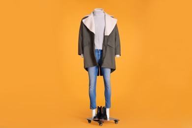 Photo of Female mannequin with boots dressed in stylish jacket, turtleneck and jeans on orange background