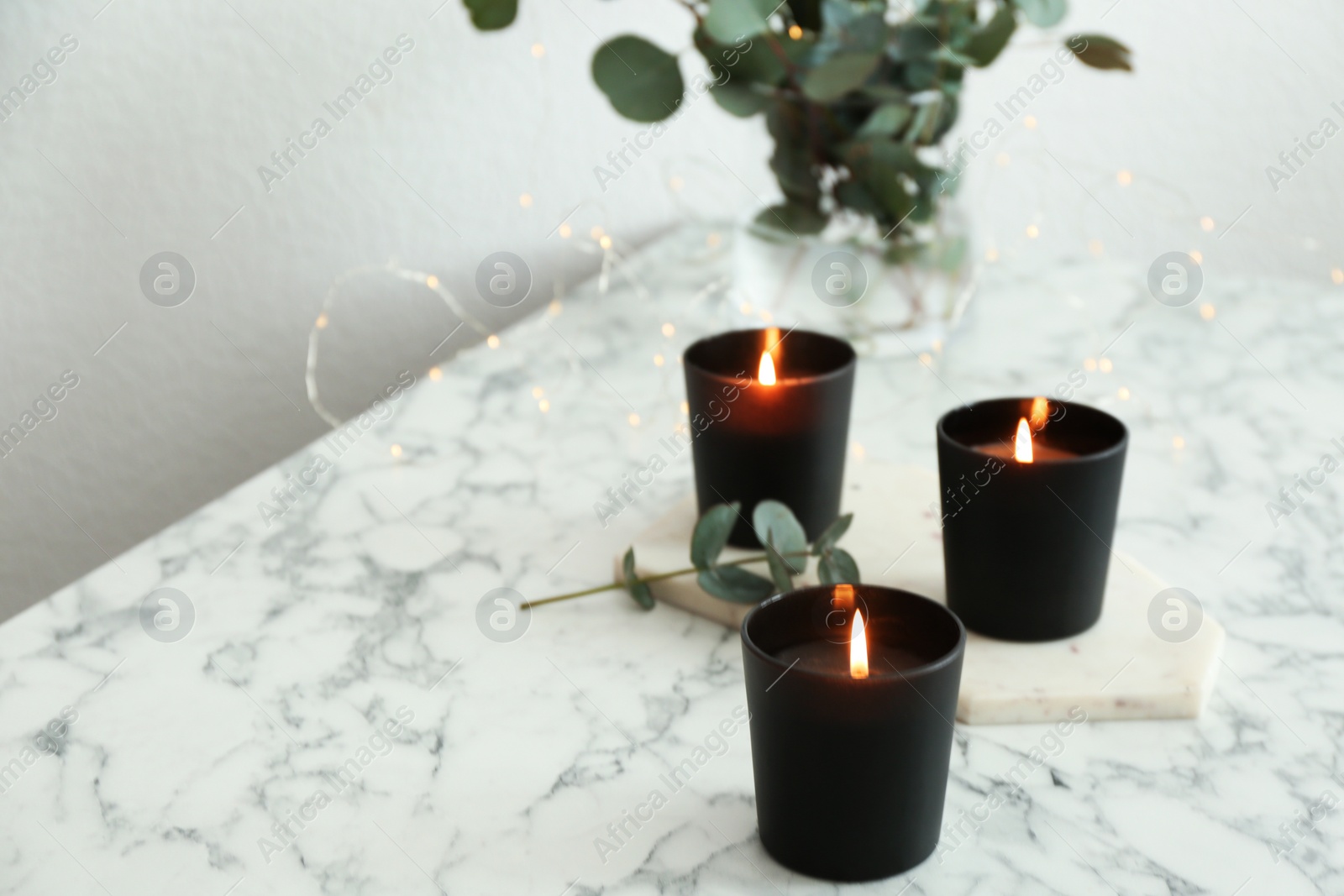 Photo of Burning candles and green branches with fairy lights on marble table