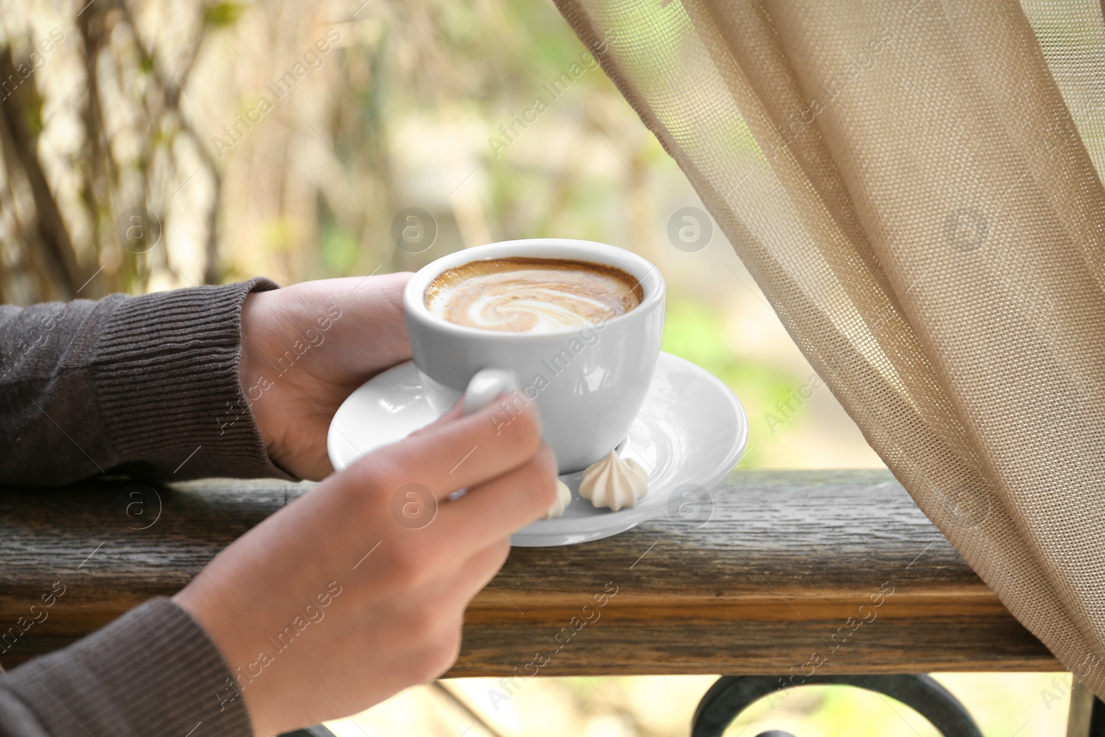 Photo of Young woman with cup of delicious coffee near window