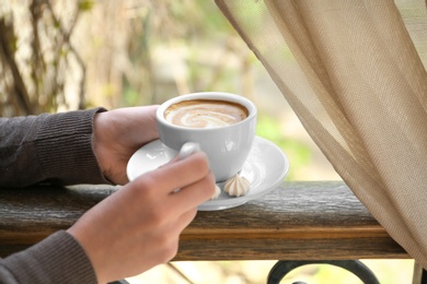 Photo of Young woman with cup of delicious coffee near window