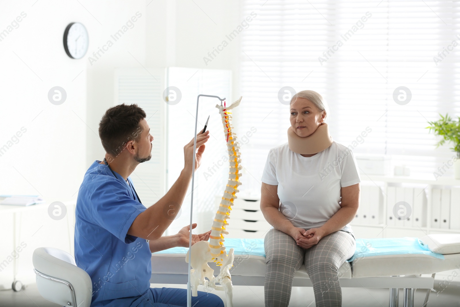 Photo of Male orthopedist explaining structure of spine to patient in clinic