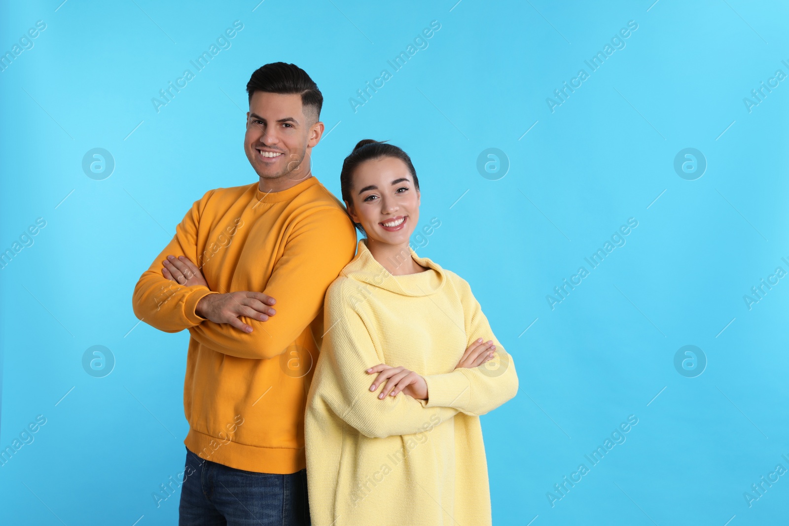 Photo of Happy couple wearing yellow warm sweaters on light blue background. Space for text