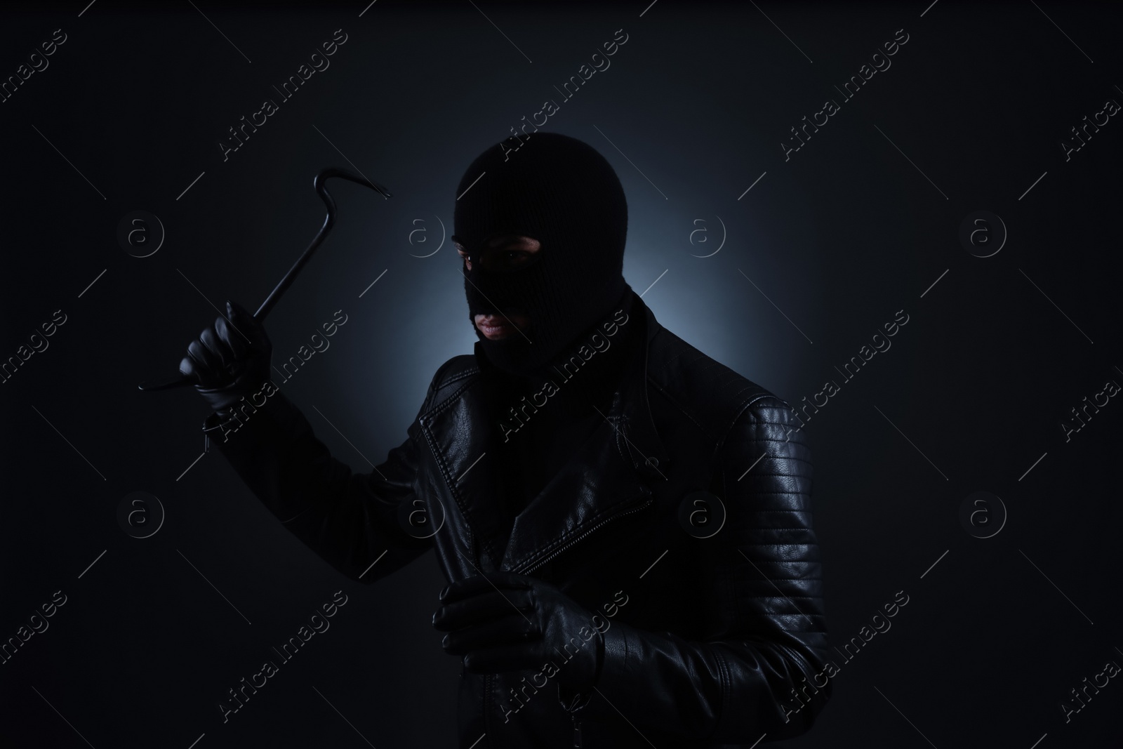 Photo of Man wearing knitted balaclava with crowbar on black background