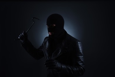 Man wearing knitted balaclava with crowbar on black background