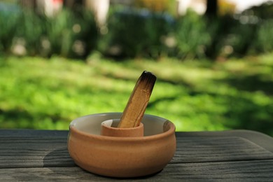 Photo of Burnt palo santo stick in holder on wooden table outdoors