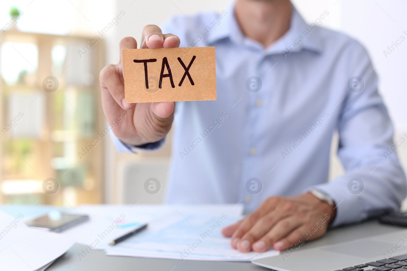 Photo of Man holding card with word TAX at table