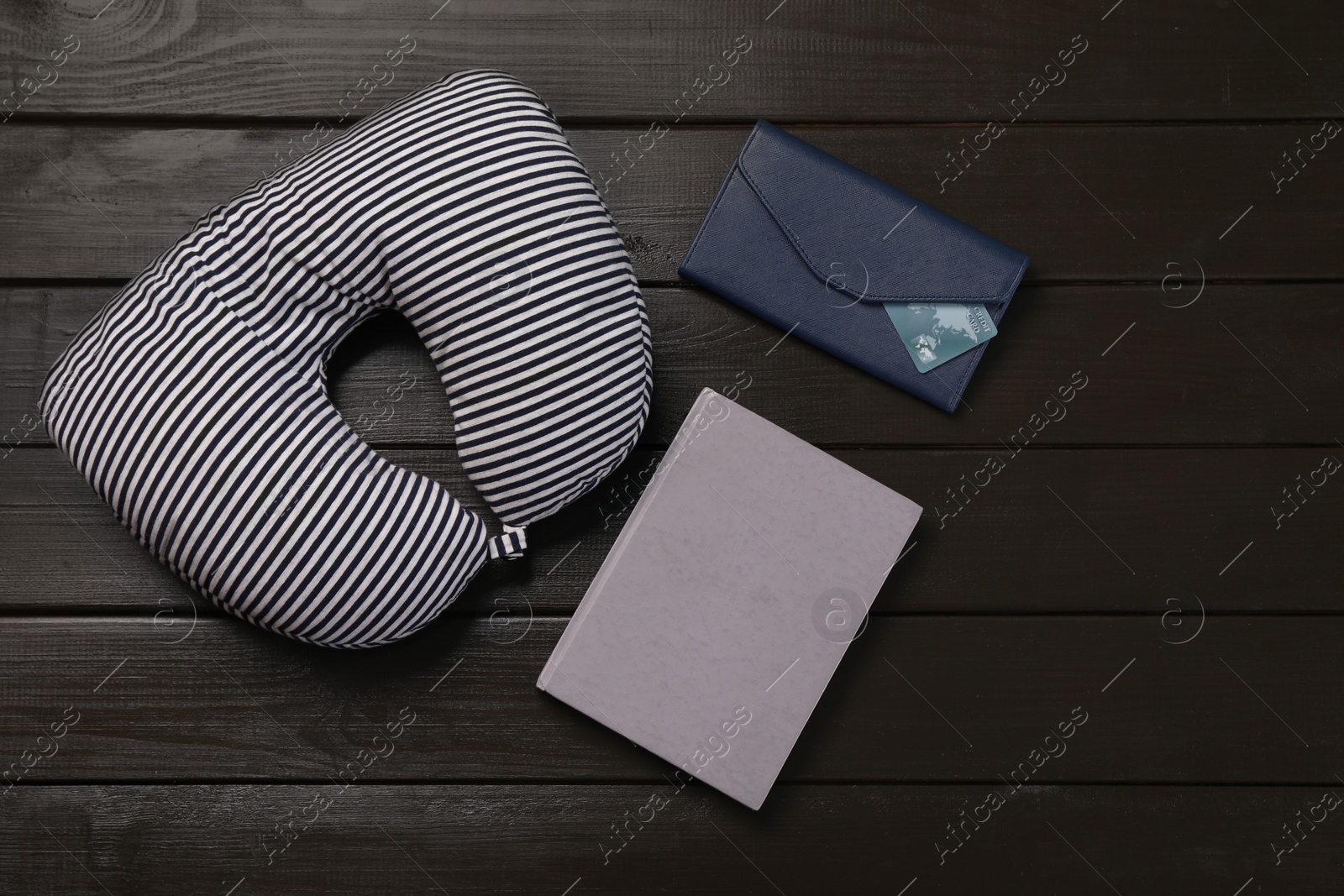 Photo of Striped travel pillow, notebook and wallet with credit card on dark wooden background, flat lay