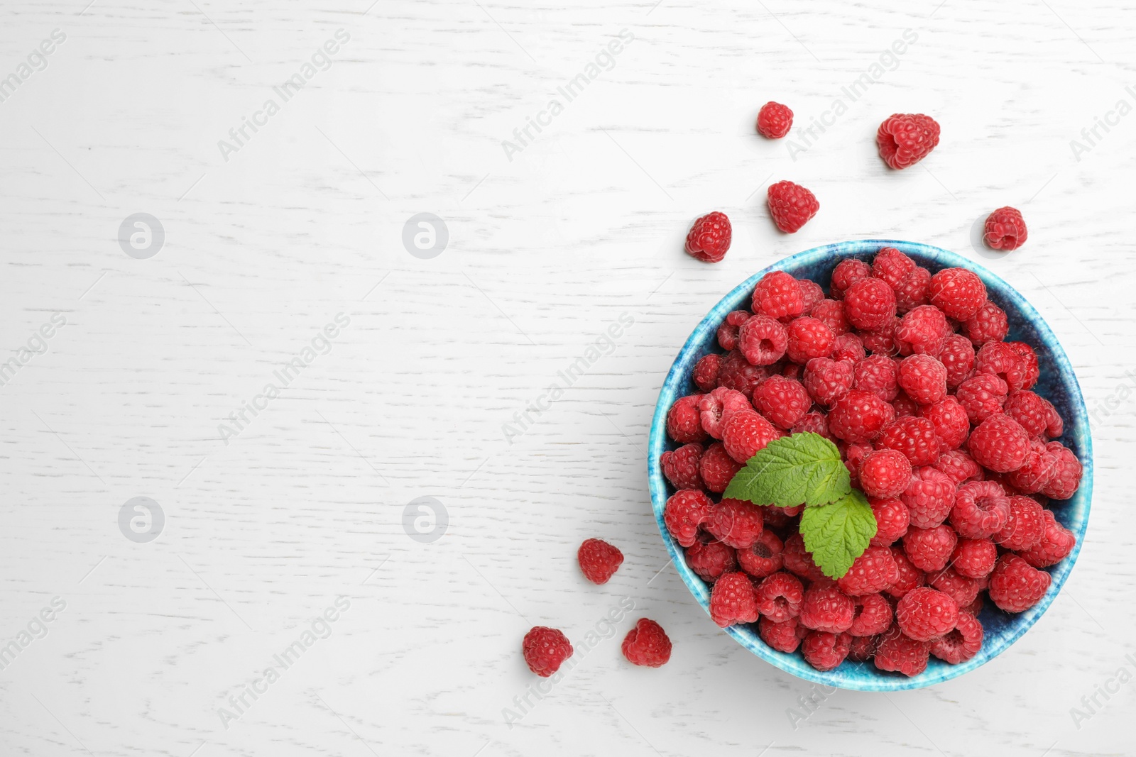 Photo of Bowl with ripe aromatic raspberries on wooden table, top view