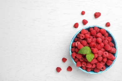 Photo of Bowl with ripe aromatic raspberries on wooden table, top view