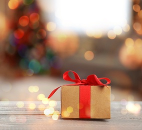 Image of Christmas gift box on wooden table against blurred background, bokeh effect