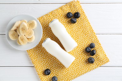 Photo of Tasty yogurt in bottles, banana and blueberries on white wooden table, top view