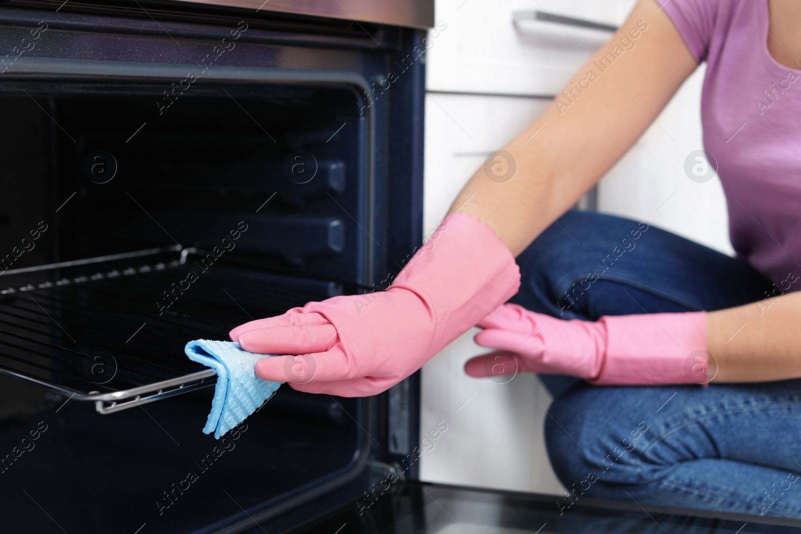 Photo of Woman cleaning oven rack with rag in kitchen, closeup